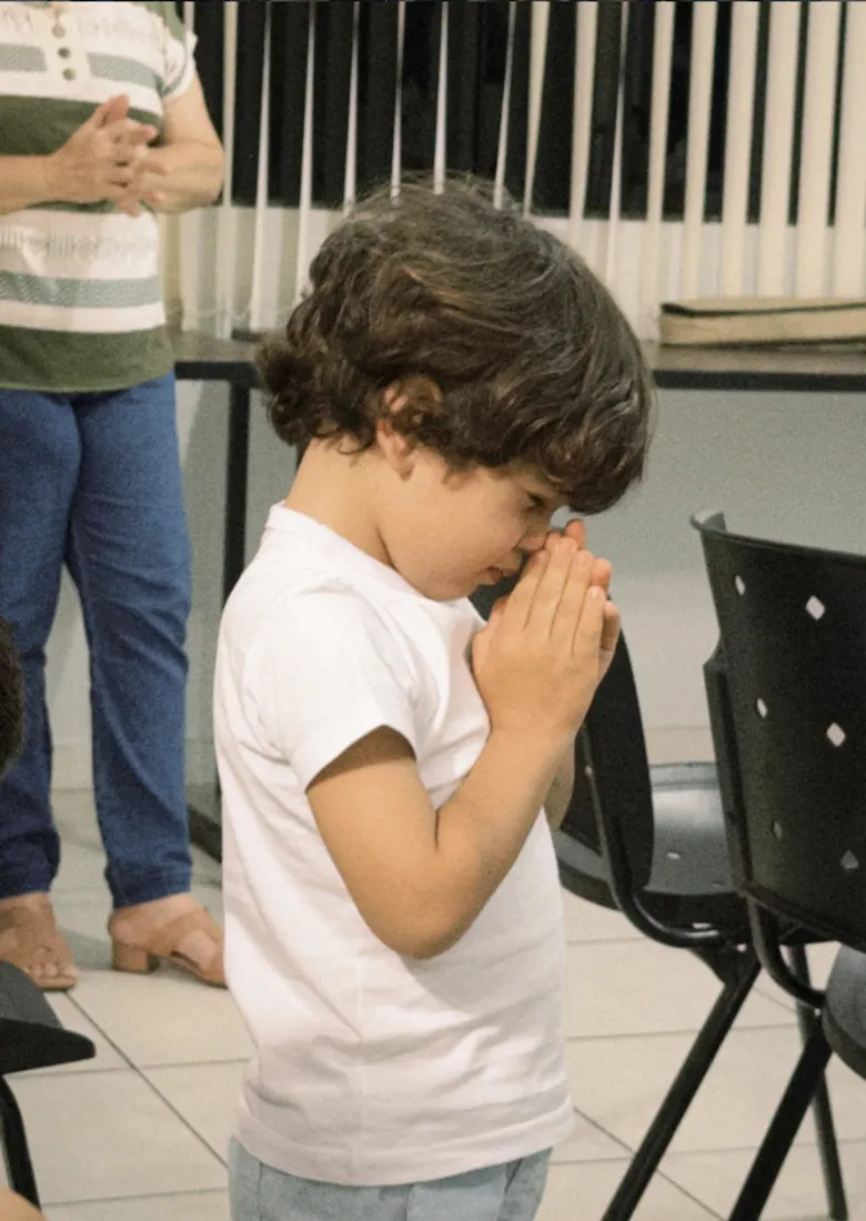Menino de olhos fechados e mãos unidas orando