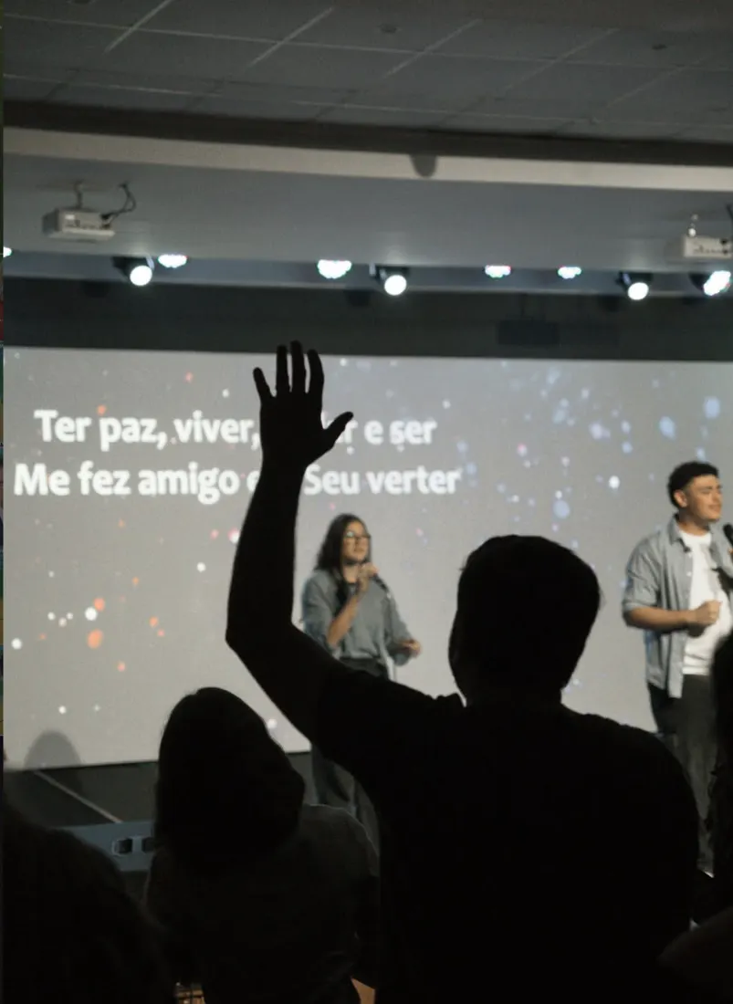 Pessoa com a mão erguida em adoração diante do telão